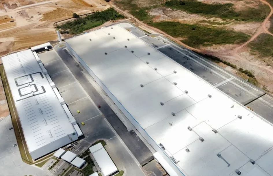 Vista aérea do centro de distribuição Amazon FOR2 em Fortaleza, Ceará, com cobertura branca de grande escala e área de expansão visível ao redor.