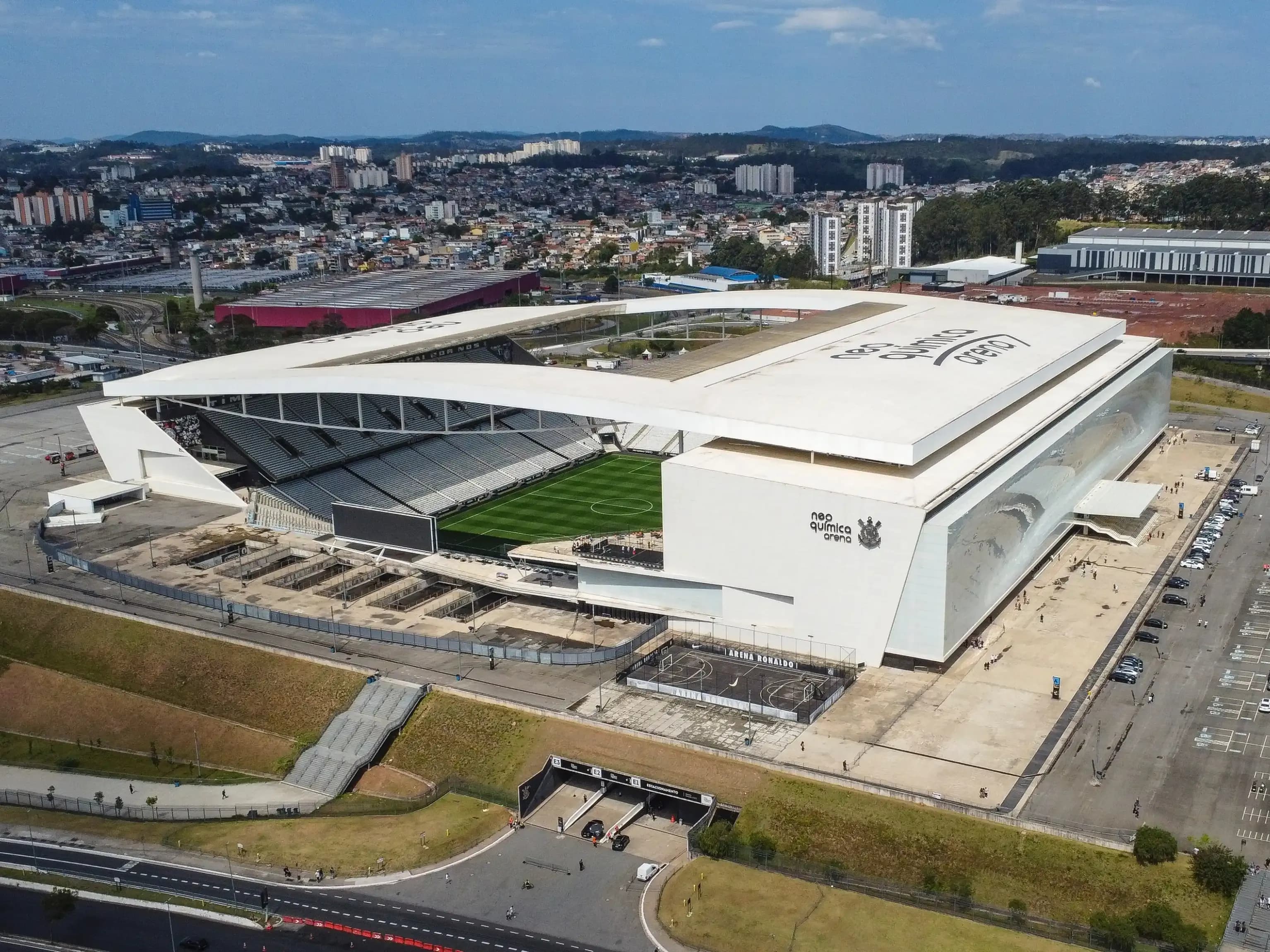 Vista aérea da Neo Química Arena, estádio do Corinthians no bairro de Itaquera, na Zona Leste de São Paulo, com cobertura branca e campo de futebol visível ao centro.